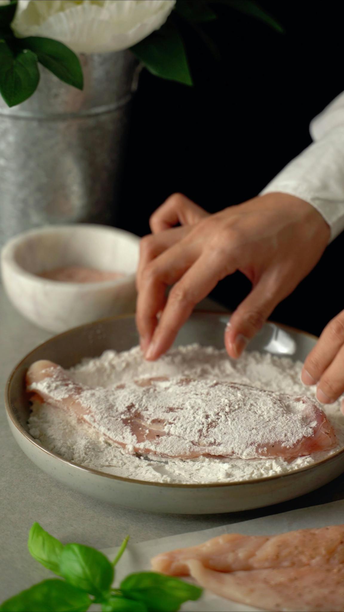 Hands coating chicken with flour in the kitchen. Perfect for cooking-themed content.