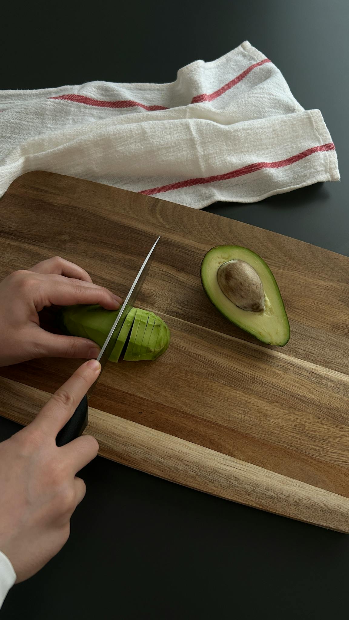 Hands cutting avocado on wooden board, showcasing healthy lifestyle.